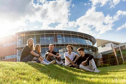 Foto: Studierende sitzen auf dem Rasen vor einem Gebäude der Technischen Hochschule Würzburg-Schweinfurt