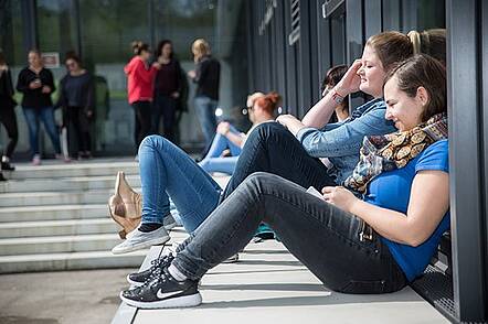 Foto: Studierende an der Hochschule für Kommunikation und Gestaltung pausieren auf dem Campus