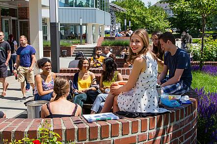 Foto: Studierende sitzen vor der Hochschule in der Sonne