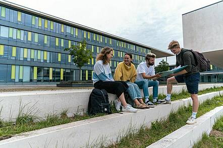Foto: Eine Gruppe Studierender sitzt auf dem Campus der Technischen Hochschule Würzburg-Schweinfurt und unterhält sich
