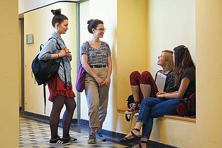 Foto: Studentinnen der Katholischen Hochschule für Sozialwesen Berlin stehen und sitzen zusammen und unterhalten sich.