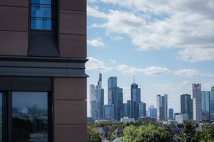 Foto: Blick auf die Fassade der Frankfurt School of Finance & Management im Vordergrund links, mit der Skyline von Frankfurt im Hintergrund