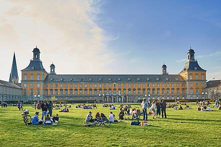 Hauptgebäude der Universität Bonn (Foto: Volker Lannert) Foto: Studierende sitzen auf der Hofgartenwiese vor dem Hauptgebäude der Universität Bonn.