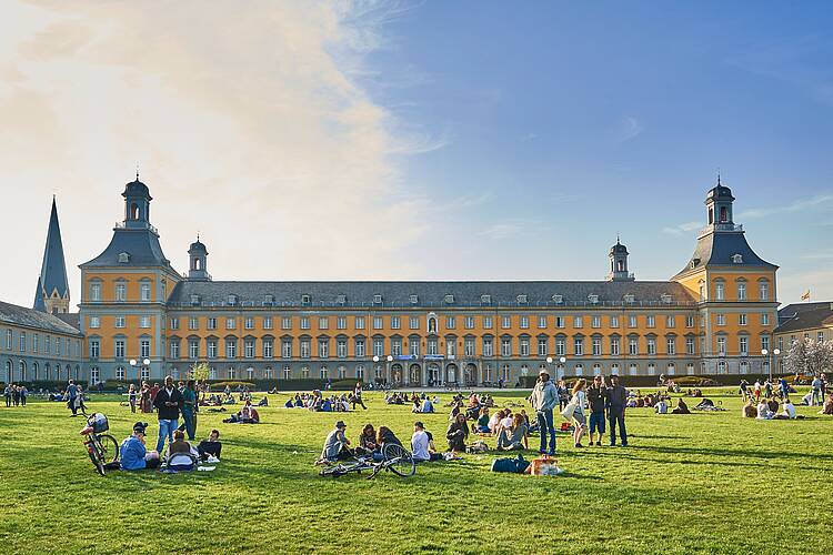 Hauptgebäude der Universität Bonn (Foto: Volker Lannert) Foto: Studierende sitzen auf der Hofgartenwiese vor dem Hauptgebäude der Universität Bonn.
