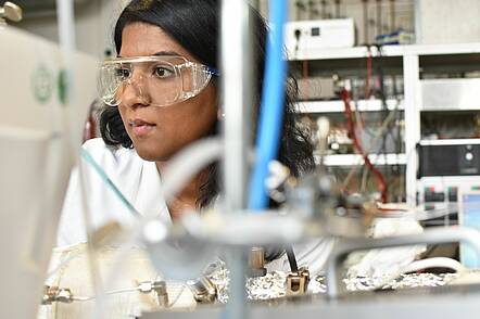 Foto: Junge Frau mit Schutzbrille in einem Forschungslabor.