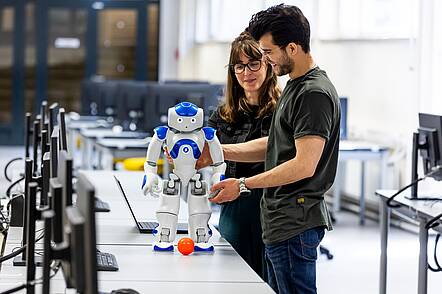 Foto: Zwei Studierende an der Universität Kassel arbeiten mit einem Roboter.