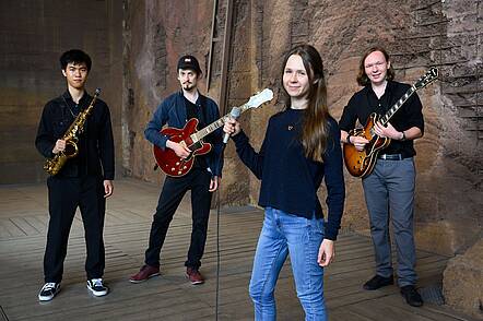 Studierende der HfM Saar im Weltkulturerbe Völklinger Hütte (Foto: Iris M. Maurer) Foto: Drei Studierende mit Gitarren und Saxophon und eine Sängerin stehen in einem Raum des Weltkulturerbes Völklinger Hütte