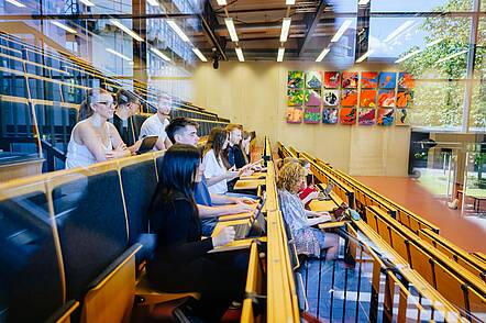 Foto: Studierende sitzen in einem Hörsaal und machen sich Notizen in ihre Laptops