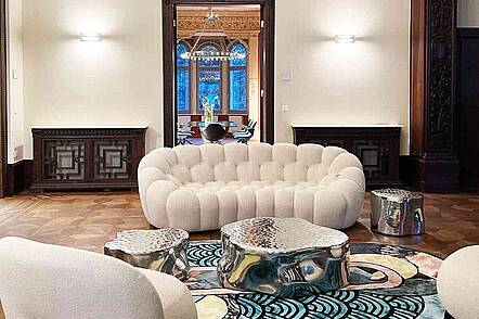 Foto: Blick in einen eleganten Wohnraum mit weißen Sitzmöbeln, einem glänzenden Tisch und einem bunten Teppich