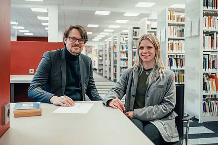 Foto: Studierende und Dozent sitzen zusammen in einer Bibliothek