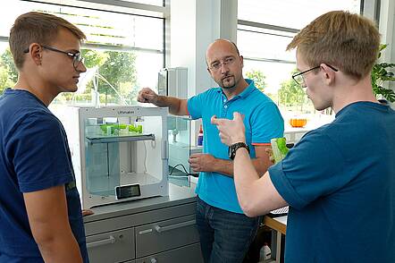 Studierende und Dozent im fachlichen Austausch (Foto: Hochschule Hof). Foto: Studierende besprechen Versuchsaufbau mit ihrem Dozenten.