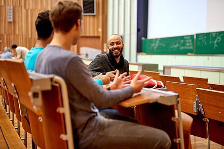 Foto: Drei Studierende sitzen im Hörsaal und unterhalten sich