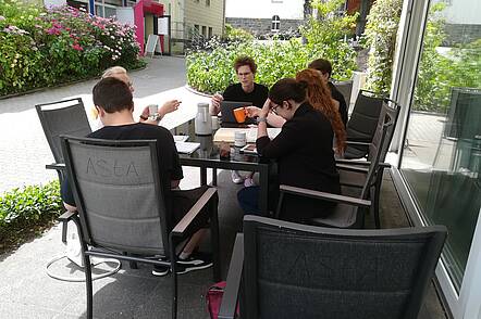 Foto: Studierende der Kirchlichen Hochschule Wuppertal sitzen vor der Cafeteria an einem Tisch und unterhalten sich