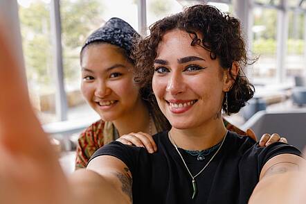 Foto: Zwei Studentinnen stehen hintereinander und machen ein Selfie