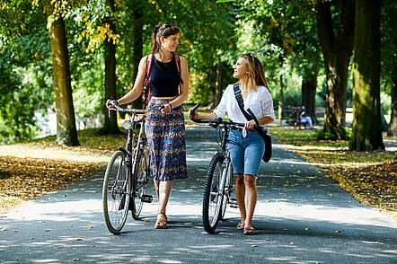 Foto: Zwei Studentinnen schieben ihre Fahrräder und unterhalten sich.