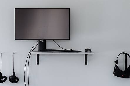 Foto: VR-Brillen sind neben einem Monitor an einer weißen Wand befestigt