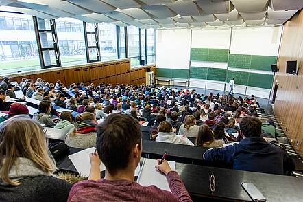 Foto: Studierende sitzen in einem vollen Hörsaal und folgen einer Vorlesung.