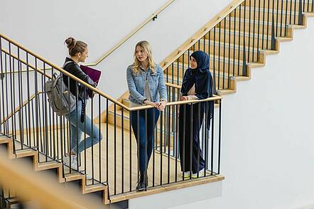 Foto: Studierende der Universität Koblenz stehen auf einer Treppe und unterhalten sich.