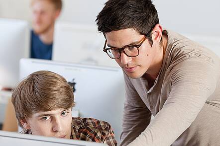 Foto: Zwei Studierende blicken auf einen Laptop und besprechen sich.