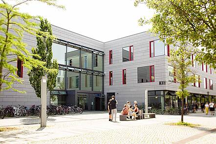 Foto: Studierende sitzen vor dem Hauptgebäude