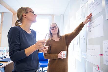 Foto: Zwei Studierende der Universität Flensburg stehen vor einem Whiteboard und betrachten Aufzeichnungen