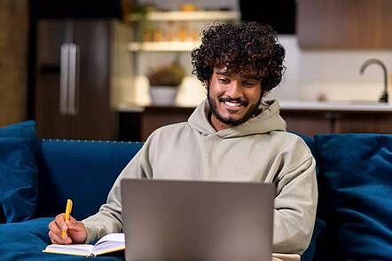 Foto: Ein Student macht sich Notizen und blickt in einen Laptop