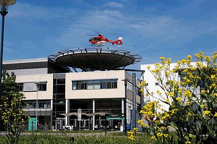 Foto: Außenansicht des Helios Klinikums in Erfurt mit einem Hubschrauberlandeplatz auf dem Dach und einem Hubschrauber darauf
