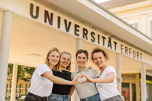 Foto: Eine Gruppe Studentinnen steht vor dem Haupteingang der Universität Erfurt