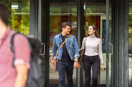 Foto: Zwei Studierende verlassen das Gebäude der TU Berlin durch eine Glastür und unterhalten sich