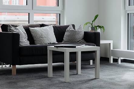 Foto: Blick auf ein gtraues Sofa und einen davorstehenden weißen Couchtisch mit Zimmerpflanze im Hintergrund