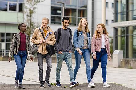 Foto: Eine Gruppe Studierender geht über den Campus der Universität Koblenz und unterhält sich.