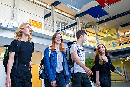Foto: Drei Studentinnen und ein Student gehen durch ein Campusgebäude der Universität Augsburg