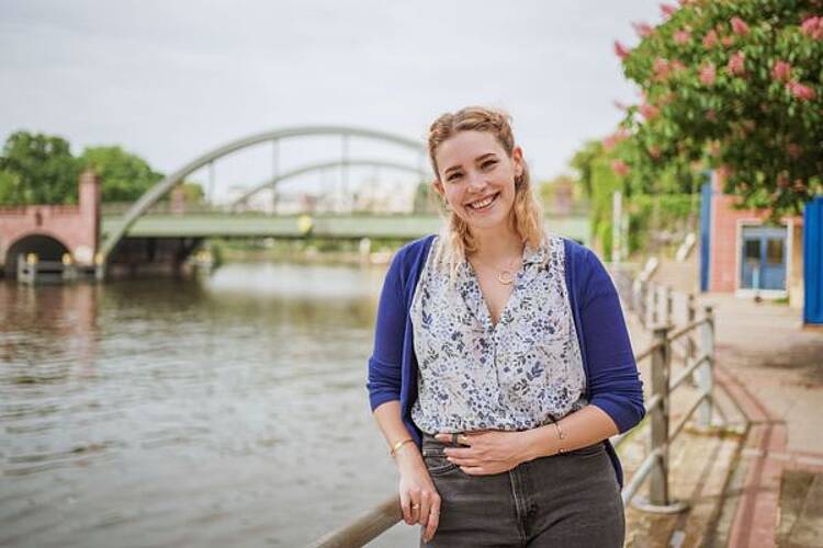 Foto: Studentin steht an einem Fluß und lächelt
