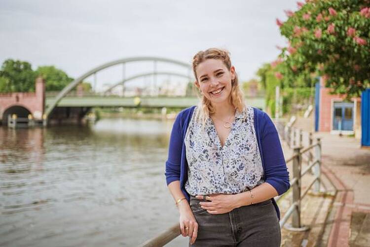 Foto: Studentin steht an einem Fluß und lächelt