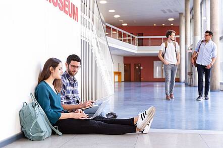 Foto: Zwei Studierende sitzen auf dem Boden eines Ganges in der TU Berlin und blicken in einen Laptop