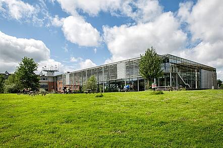 Foto: Blick über eine grüne Wiese auf das Hochschulgebäude der Universität Flensburg