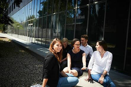 Foto: Studierende sitzen auf dem Campus vor der Technischen Hochschule Ingolstadt und unterhalten sich. 