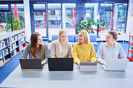 Foto: Vier Studentinnen sitzen gemeinsam an ihrem Laptops in der Bibliothek.