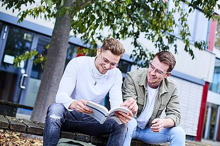 Foto: Zwei Studenten der Hochschule Kehl sitzen zusammen über einem Buch.