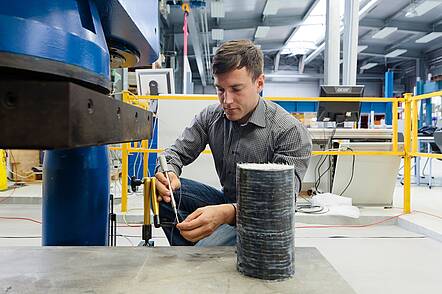 Foto: Studierender trifft letzte Vorbereitungen für einen Belastungstest an einem carbonfaserverstärktem Probekörper in der Bauversuchshalle der Hochschule