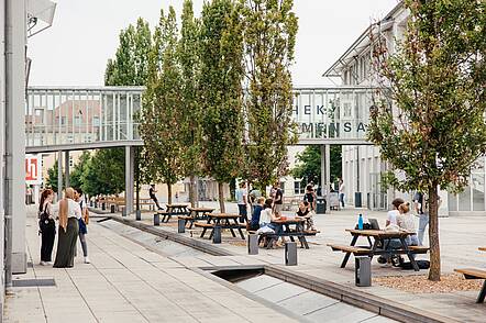 Foto: Blick über den Campus der Hochschule Landshut, auf dem Studierende an Tischen sitzen oder in Gruppen zusammenstehen