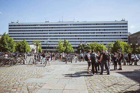 Foto: Blick über den Campus, auf dem Studierende stehen, auf das Gebäude der TU Berlin