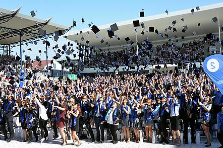 Foto: Graduierte feiern im Freien und werfen ihre Doktorhüte in die Luft