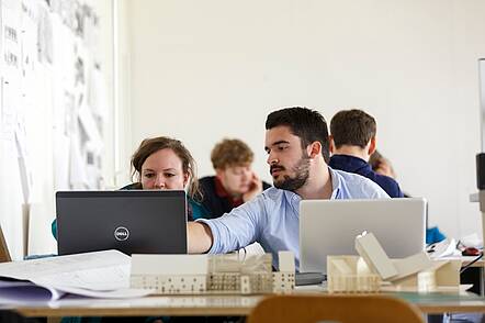 Studierende der Fakultät Architektur der OTH Regensburg (Foto: Florian Hammerich) Foto: Studierende der Fakultät Architektur sitzen vor ihren Laptops und einem Modell und arbeiten an einer Projektarbeit