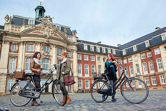 Foto: Studierende stehen mit ihren Fahrrädern auf dem Schlossplatz der Universität Münster.
