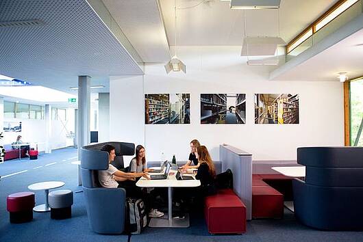 Foto: Vier Studierende sitzen an einem Tisch auf dem ihre Laptops stehen und unterhalten sich