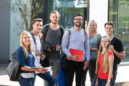 Foto: Eine Gruppe Studierender steht auf dem Campus und blickt in die Kamera.