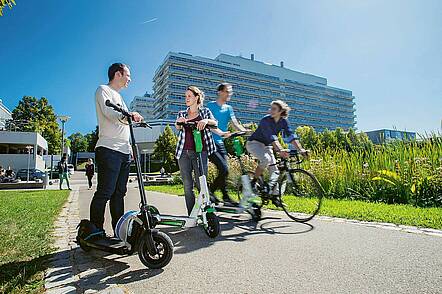 Foto: Studierende bewegen sich mit dem E-Scooter auf dem Campus der Universität Stuttgart.