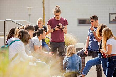 Foto: Eine Gruppe Studierender sitzt auf dem Campus und unterhält sich.   