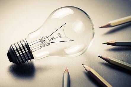 Foto: Glühbirne auf einem Tisch mit Bleistiften, die auf die Glühbirne ausgerichtet sind